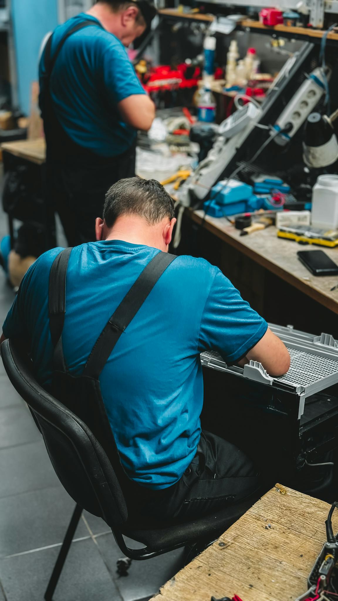 Two technicians repairing electronic devices in a cluttered workshop.